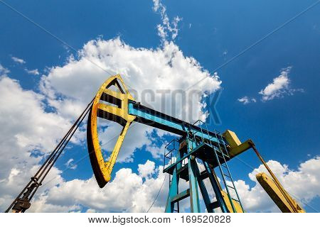 Oil field with pump jack, profiled on blue sky with white clouds, on a sunny day in spring