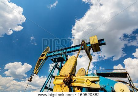 Oil field with pump jack, profiled on blue sky with white clouds, on a sunny day in spring