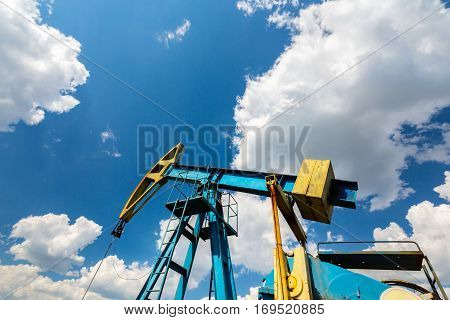 Oil field with pump jack, profiled on blue sky with white clouds, on a sunny day in spring