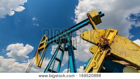 Oil field with pump jack, profiled on blue sky with white clouds, on a sunny day in spring