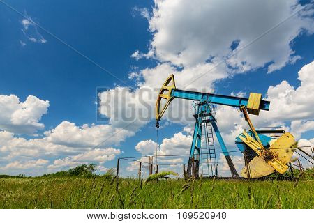 Oil field with pump jack, profiled on blue sky with white clouds, on a sunny day in spring