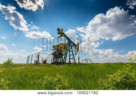 Oil field with pump jack, profiled on blue sky with white clouds, on a sunny day in spring