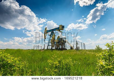 Oil field with pump jack, profiled on blue sky with white clouds, on a sunny day in spring
