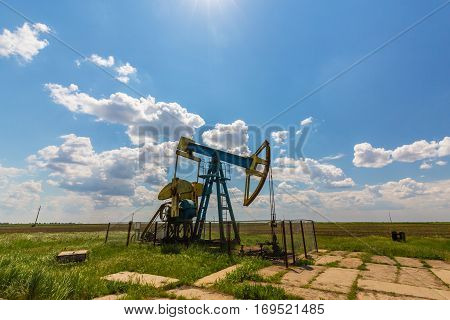 Oil field with pump jack, profiled on blue sky with white clouds, on a sunny day in spring