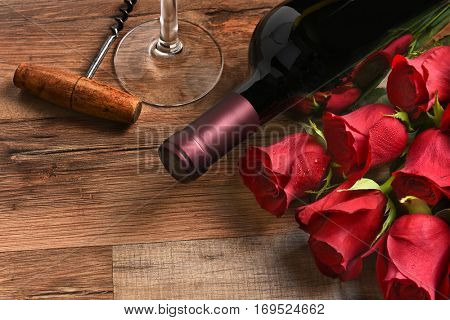 Valentines Day still life. A wine bottle with red roses and a glass and cork screw on a rustic wood table with copy space.