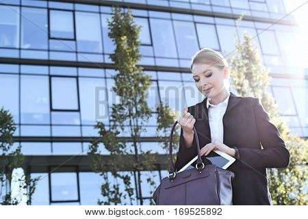 Businesswoman putting digital tablet in purse on sunny day