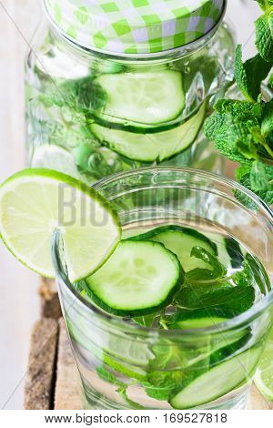 Glass and jar mug with infused detox cucumber water with lime and fresh mint close up cleansing spring