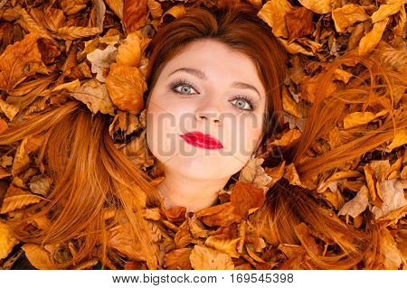Nature concept. Beautiful girl between leaves. Autumn in the park. Young lady is enjoying good weather. Looking straigh ahead.