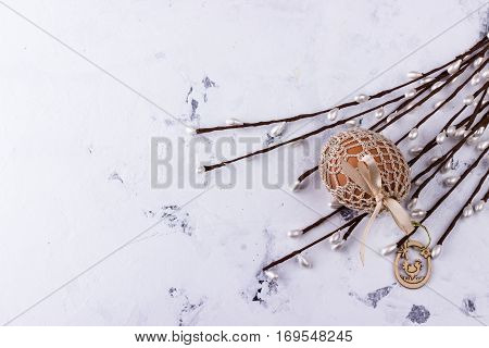 Easter egg in knitted bag on white marble background with spring decoration of easter symbols and willows.