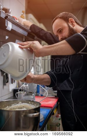 Preparing cream in restaraunt or cafe kitchen. Male chef in black uniform cooking dessert.