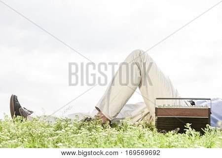 Low section of man lying by vintage radio on grass against clear sky