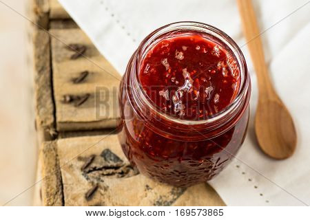 Jar with homemade raspberry jam with wooden spoon, on white linen napkin, top angle view,cozy morning atmosphere,breakfast
