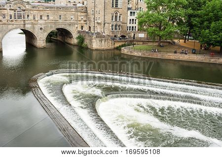 Bath, Somerset, United Kingdom - June 19, 2006: People relaxing in the park near the Pulteney Bridge. The Pulteney Bridge (Georgian architecture) over the river Avon with weir in Bath.