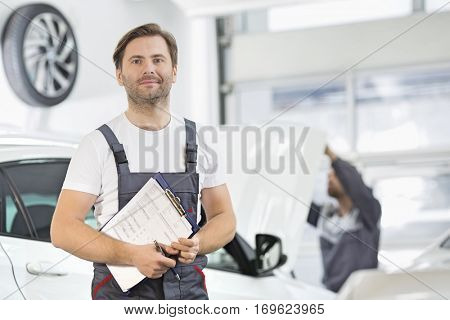 Portrait of confident male maintenance engineer with clipboard in car repair shop