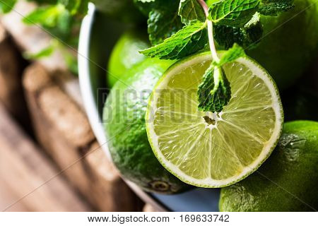 Heap of ripe organic limes cut in half in the sunlight, leaves of fresh mint, on vintage wood, ingredients for infused detox drinks, citrus, cleansing, diet,freshness, health concept