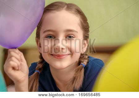 Smiling cute little girl lying on bed with balloons. Closeup portrait.