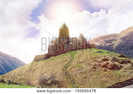 Gergeti Trinity Church Or Tsminda Sameba in the morning mist near village Stepantsminda, Georgia. Mount Kazbegi. Spring Or Summer Season.