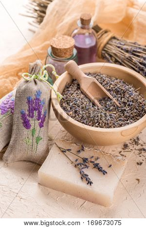 Wooden bowl with petals of lavender bottles of aromatic oil and salt sachets with embroidery homemade soap and dried lavender bouquet