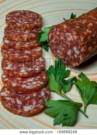 Smoked sausage salami sliced on a plate with greens.