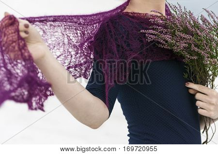 Unrecognizable model demonstrates knitted crochet scarf. Closeup view of scarf and heather flowers  holding hands.