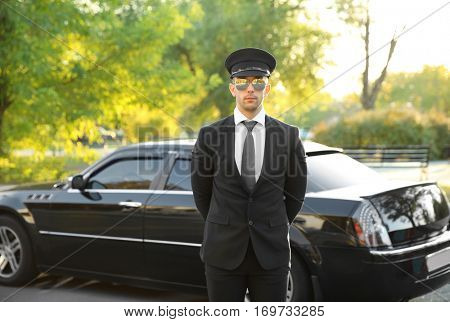 Young chauffeur standing near luxury car on the street