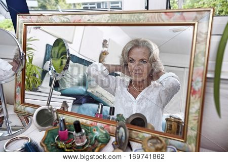 Mirror reflection of senior woman putting on necklace at home