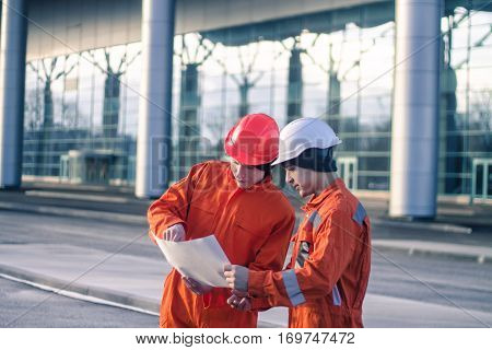 team of young engineers discussing a construction project. The wear overalls and safety helmets. Business modern background