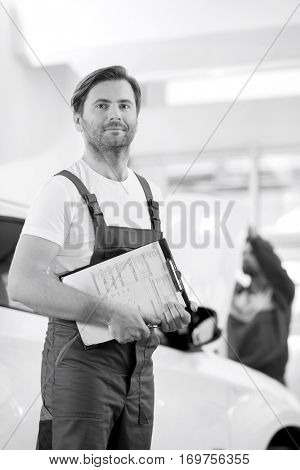 Portrait of confident male automobile mechanic with clipboard in car repair store