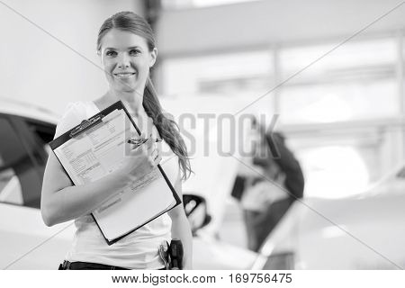 Portrait of smiling female repair worker with clipboard in car workshop