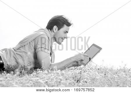 Side view of young man using digital tablet while lying on grass against clear sky