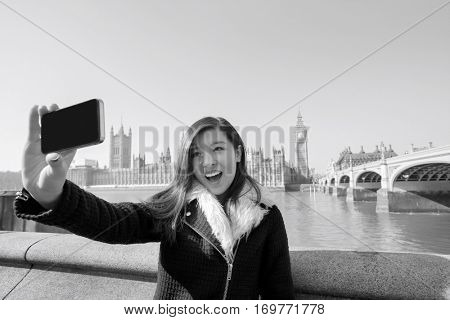 Happy young woman taking self portrait through cell phone against Big Ben at London; England; UK