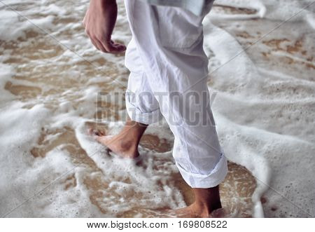 Male legs in sandy foam shore of ocean