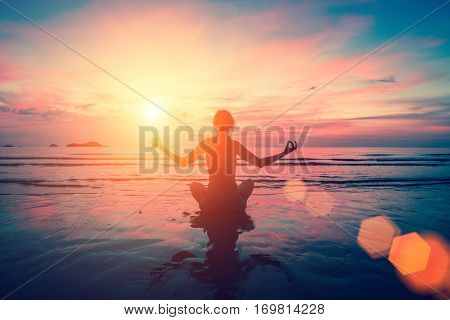 Silhouette young woman practicing yoga on the sea beach at surrealistic bloody red sunset.