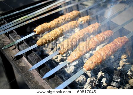 Spits with luleh kebab on the grill over hot coals, close-up