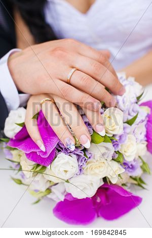 Wedding rings on couple hands on bridal bouquet. Engagement rings on just married bride and groom hands. Golden female and male rings. Jewelry accessory for wedding day. Symbol of eternal love