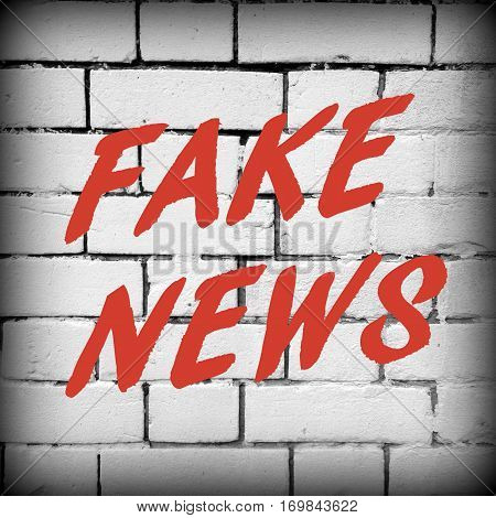The words Fake News in red text on a white brick wall as a reminder to be aware of hoaxes and disinformation for propaganda uses