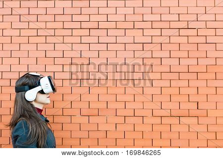 Handsome young woman using VR glasses with brickwall background and space for text