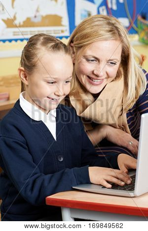 Teacher Helping Female Elementary School Pupil In Computer Class