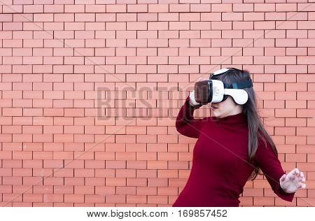 Handsome young woman using VR glasses with brickwall background and space for text