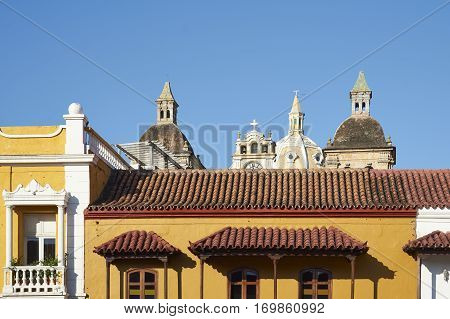Towers and dome of the Iglesia de San Pedro Claver rise above the rooftops of historic buildings surrounding the Plaza De La Aduana in the Spanish colonial city of Cartagena de Indias, Colombia.