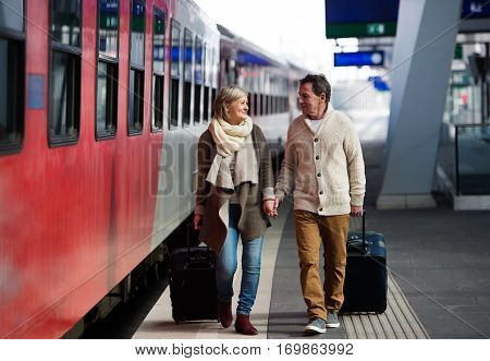 Beautiful senior couple on trainstation pulling a trolley luggage.