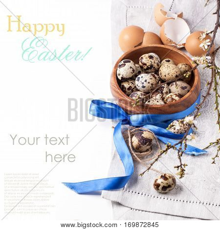 Easter background with wooden bowl of quail eggs, blossom branch and eggshells over white with sample text.