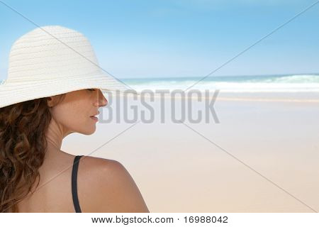 ผู้หญิงสวยงามนั่งอยู่บนชายหาดกับหมวกฟาง