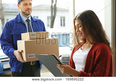 Young woman signing documents after receiving parcels from courier