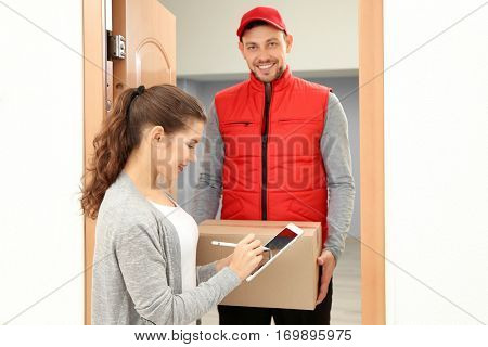 Young woman appending signature after receiving parcel from courier at home