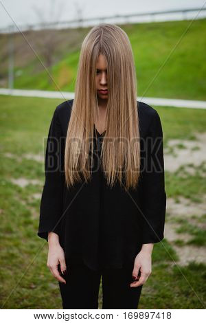 Blond girl with long blonde hair covering her face in the park