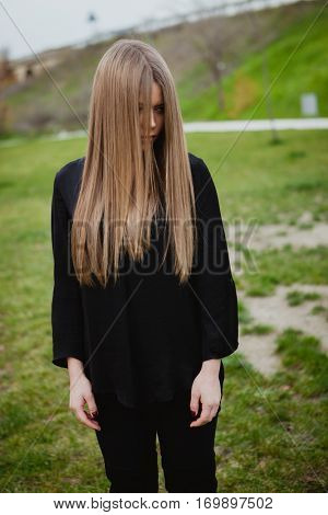 Blond girl with long blonde hair covering her face in the park