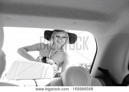 Happy woman loading suitcase in car trunk