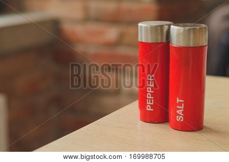 Red plastic salt cellar and pepperbox on a wooden table on loft brickwall background faded colors