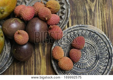 Tropical fruits - Lychees and Passion Fruit or Maracuya and Mango on wooden background